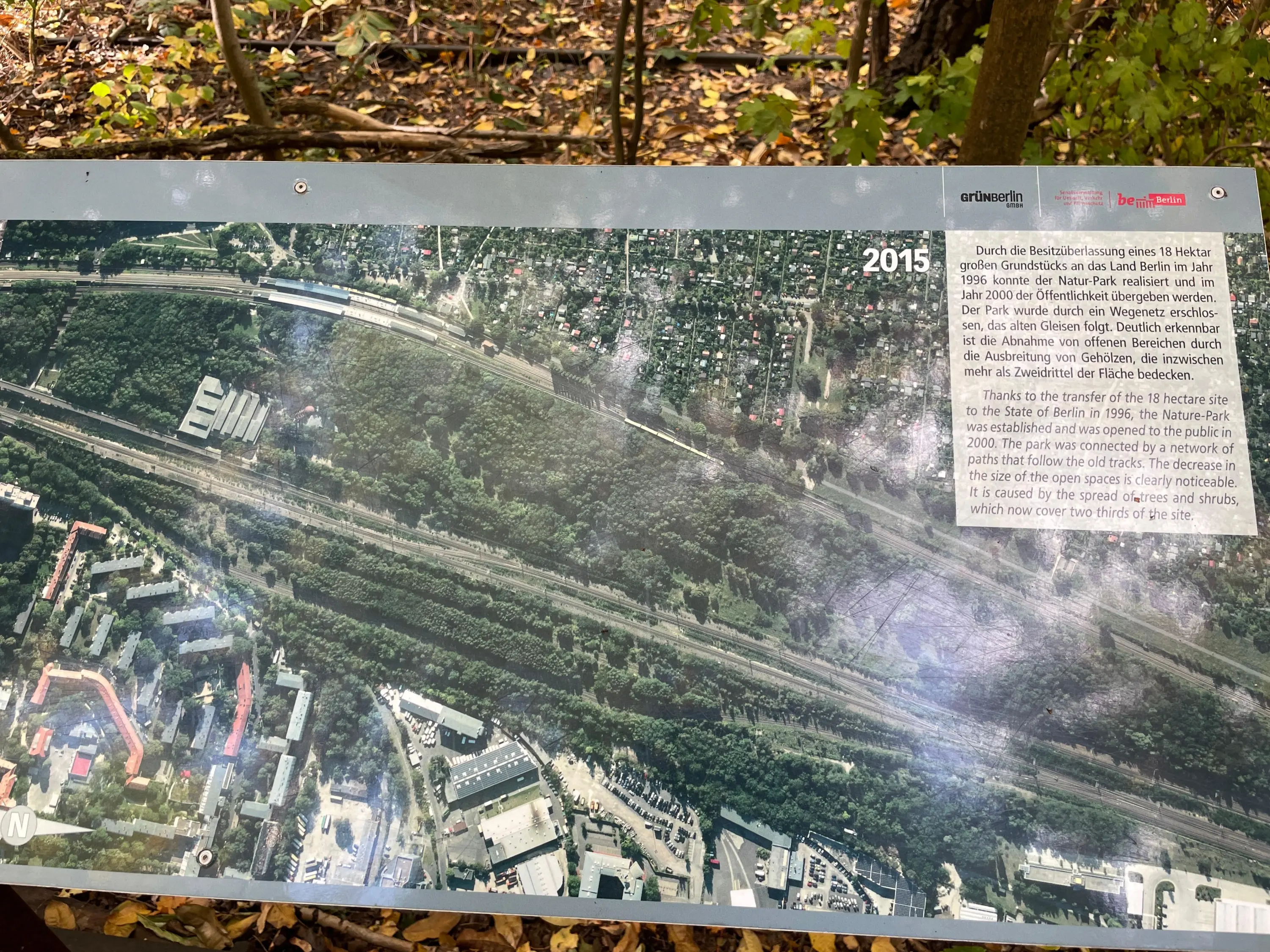 Informationstafel mit Luftbild von 2015 zeigt bewaldetes Gebiet und umliegende Wohn- und Industriegebiete im Natur-Park Berlin.